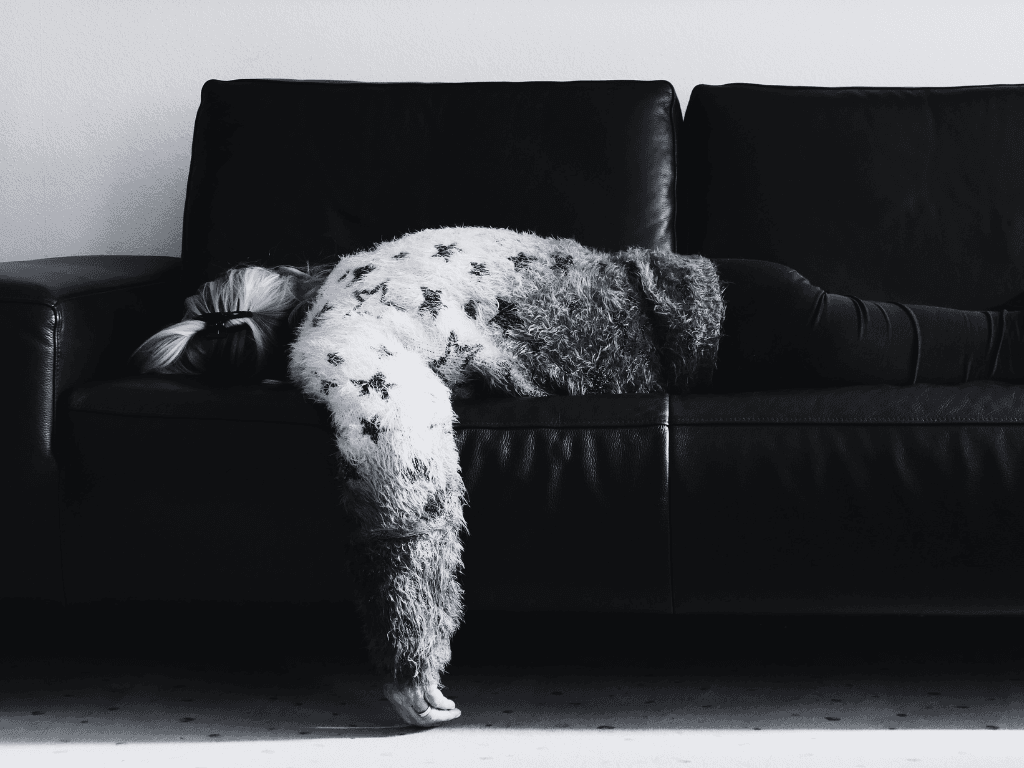 A person slumped exhausted on a black leather sofa, representing consumer digital fatigue