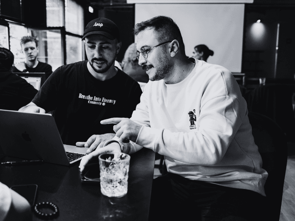 Two people collaborating over a laptop in a coffee shop, representing mentorship and support in leadership