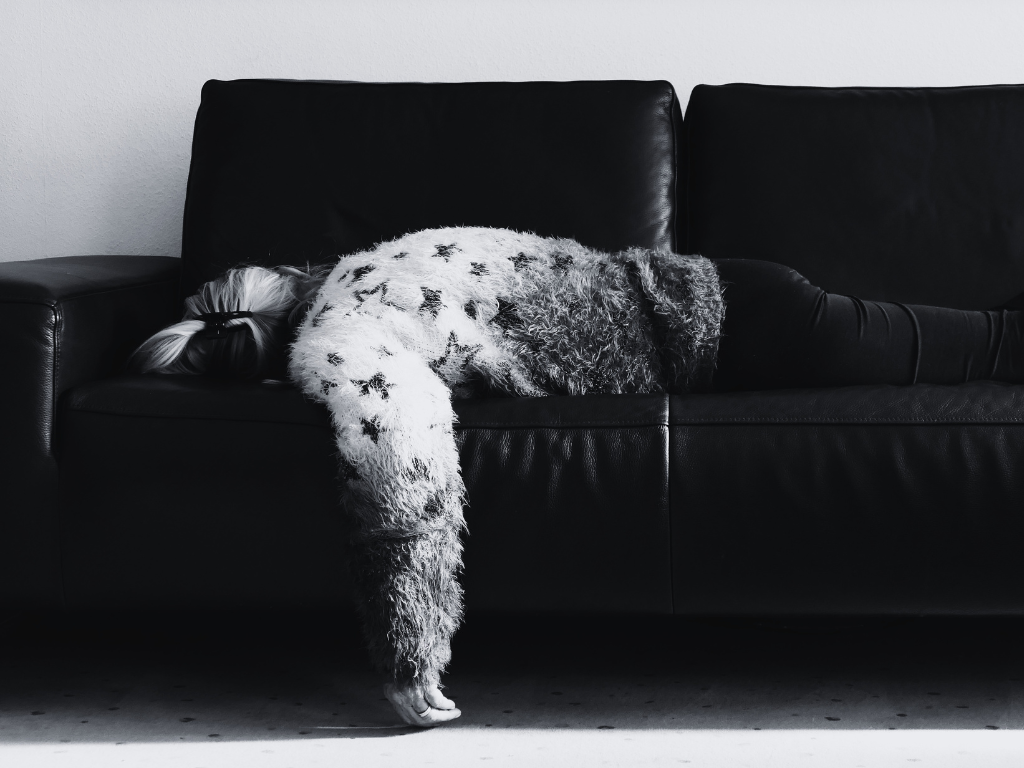 A person slumped exhausted on a black leather sofa, representing consumer digital fatigue