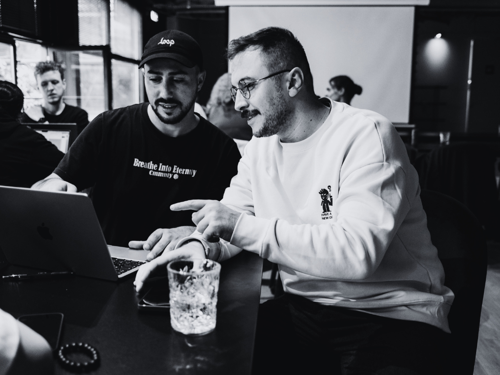 Two people collaborating over a laptop in a coffee shop, representing mentorship and support in leadership