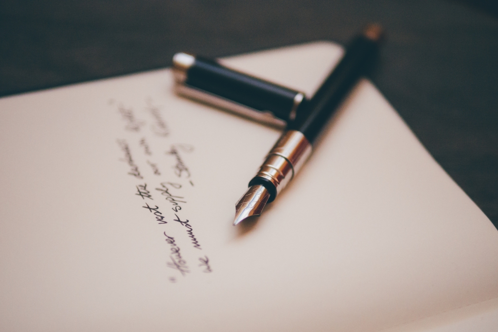 A fountain pen resting on a handwritten note on cream paper